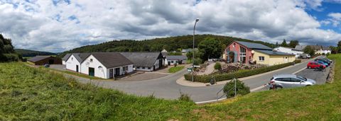 <p>Panorama der ländlichen Gegend rund um den Gröner Hof mit mehreren Gebäuden, einer Straße und parkenden Autos. Im Hintergrund sind bewaldete Hügel zu sehen.</p>