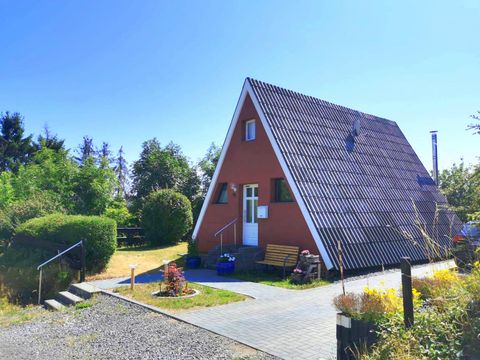 Ein gemütliches, rot getünchtes Ferienhaus mit einem Satteldach. Umgeben von grünen Büschen und einem klaren blauen Himmel.