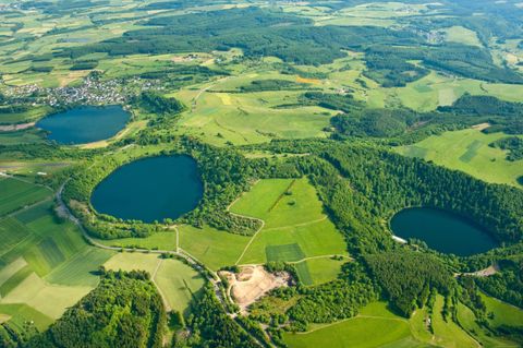 Luftaufnahme von grünen Feldern mit zwei blauen Seen. Umgeben von Wäldern und sanften Hügeln.