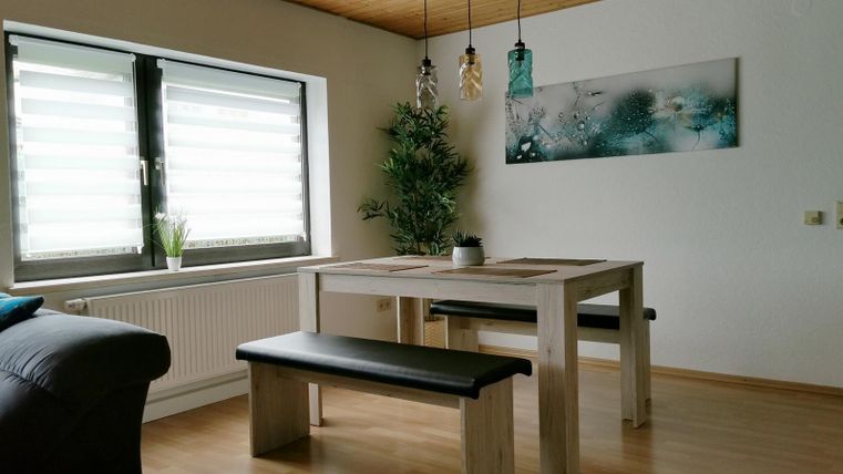 Ein modernes Esszimmer mit einem hellen Holztisch und Bänken. Große Fenster sorgen für viel Tageslicht und eine schöne Wanddekoration ergänzt den Raum.