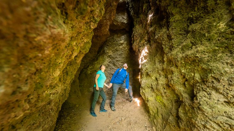 Zwei Personen in einer schmalen, felsigen Höhle, die nach oben schauen.