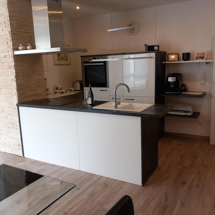 A modern kitchen with a central island and stylish, minimalist design. The space is bright and well-equipped with cooking appliances.