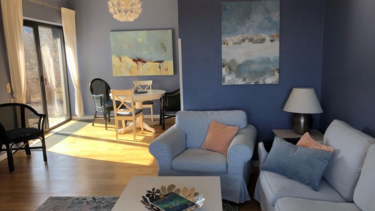 Ein modernes Wohnzimmer mit einem weißen Sofa und einem Couchtisch. Die Wände sind in einem sanften Blauton gestrichen, und es gibt viel Tageslicht durch die Fenster.