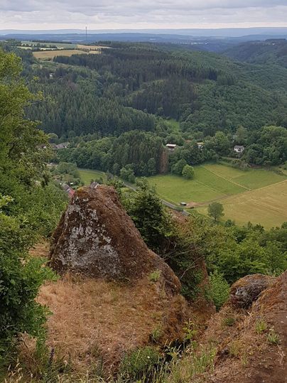 Eine schöne Aussicht auf grüne Hügel und Wälder. Im Hintergrund sind Felder und ein kleines Dorf sichtbar.