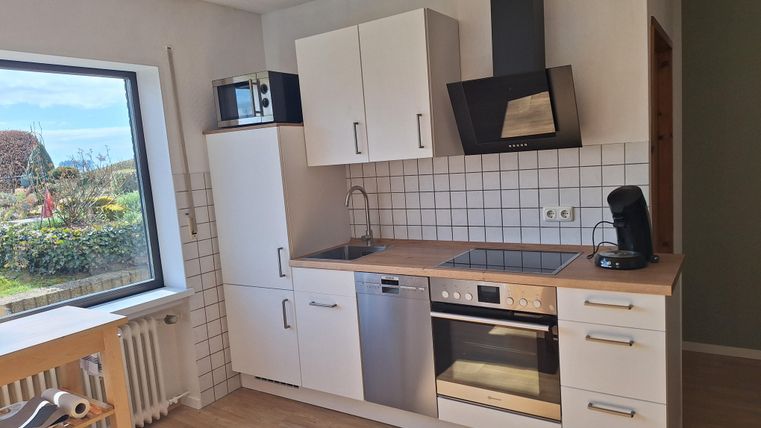 Eine moderne Küche mit weißen Schränken und einem Holzarbeitsplatz. Durch das Fenster ist eine grüne Landschaft sichtbar.