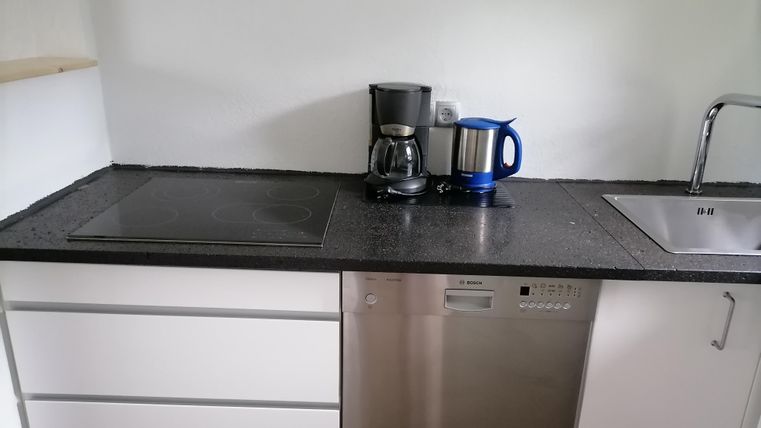 Eine moderne Küche mit einem schwarzen Arbeitsbereich. Auf der Arbeitsfläche stehen eine Kaffeemaschine, ein Wasserkocher und eine Spüle.