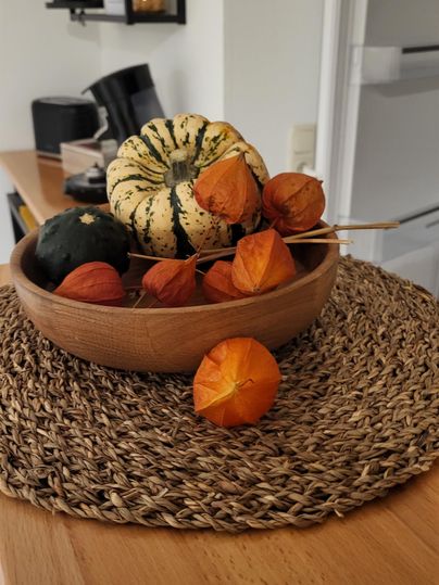 Eine Schüssel mit bunten Kürbissen und Physalis auf einem geflochtenen Platz. Der Tisch hat eine moderne gemütliche Atmosphäre.