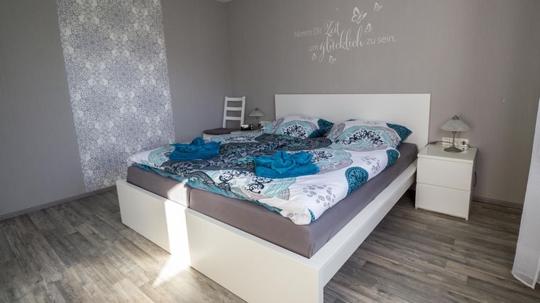 Ein gemütliches Schlafzimmer mit einem großen Bett und bunten Bettwäsche. Der Raum hat helle Wände und einen modernen Holzfußboden.