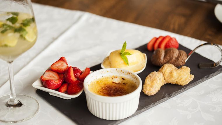 Ein Dessertteller mit Crème brûlée, frischen Erdbeeren und verschiedenen kleinen Süßspeisen. Dazu ein erfrischendes Getränk in einem Glas.