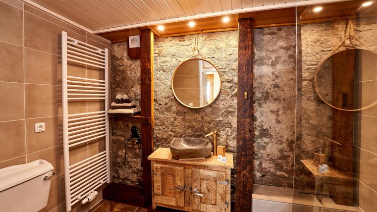 Ein modernes Badezimmer mit Holz- und Steinelementen. Es ist gut beleuchtet und verfügt über einen runden Spiegel sowie eine stilvolle Waschbeckenanlage.