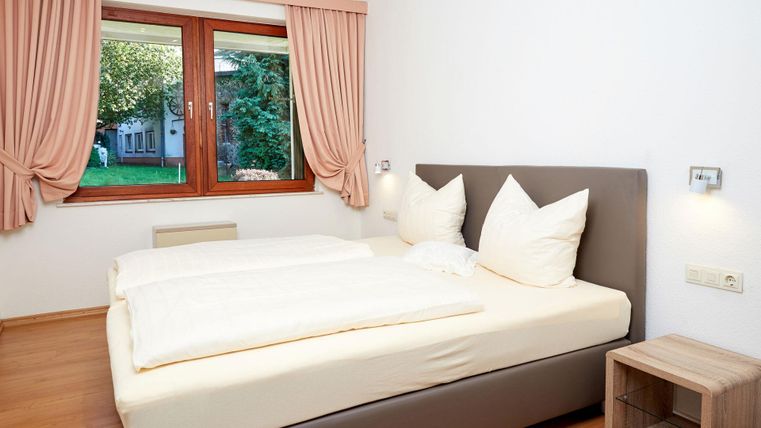 Ein gemütliches Schlafzimmer mit einem Doppelbett und großen, weißen Kissen. Durch das Fenster sieht man einen grünen Garten.