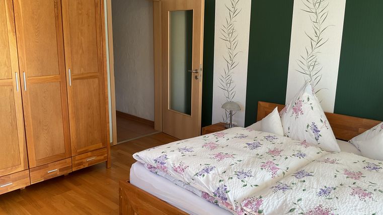 Ein gemütliches Schlafzimmer mit einem Holzschrank und einem Doppelbett. Die Wände sind grün gestrichen und mit Pflanzenmotiven dekoriert.