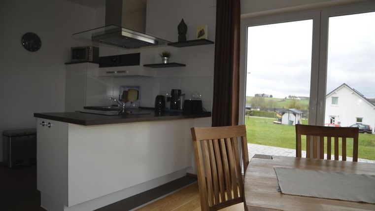 Eine moderne Küche mit einem Tisch und Stühlen. Durch große Fenster ist der Blick auf die grüne Landschaft sichtbar.