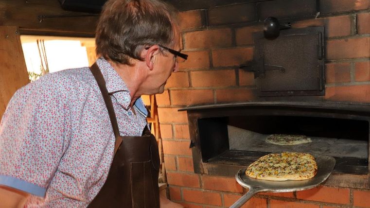 Ein Mann holt eine frisch gebackene Pizza aus einem Holzofen. Der Ofen hat eine rustikale Backsteinoberfläche.