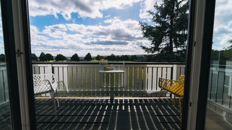 Ein schöner Balkon mit einem Tisch und zwei Stühlen. Der Himmel ist klar, und die Landschaft ist grün.