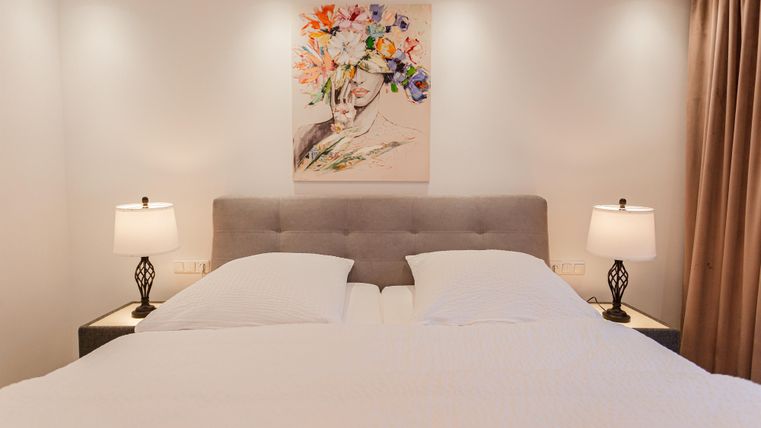 Ein modernes Schlafzimmer mit einem großen Bett und zwei Nachttischen. An der Wand hängt ein Gemälde mit bunten Blumen.