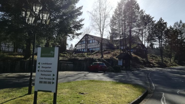 Ein malerisches Gebäude inmitten von Bäumen. Die beschilderte Zufahrt zeigt den Weg zu verschiedenen Einrichtungen.