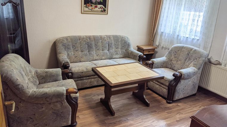 Ein gemütliches Wohnzimmer mit einem beigen Sofa und einem Sessel. Ein kleiner Tisch aus Holz steht in der Mitte.