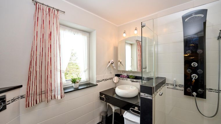 Ein modernes Badezimmer mit Dusche und Spiegel. Helle Wände und ein großes Fenster sorgen für eine freundliche Atmosphäre.