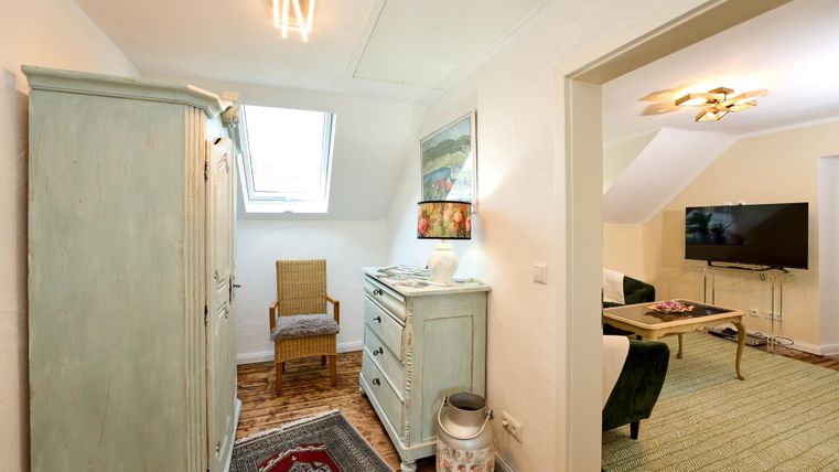 Ein gemütlicher Flur mit einem hellgrünen Schrank und einem Stuhl. Im Hintergrund ist ein Wohnbereich mit Sofa und Fernseher sichtbar.