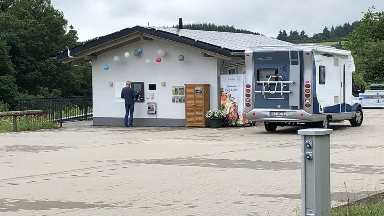 Ein Wohnmobil parkte vor einem kleinen, modernen Gebäude. Eine Person steht vor einem Informationsschalter.