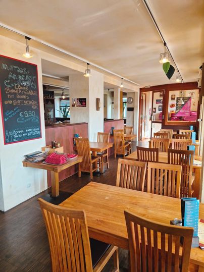 Ein gemütliches Restaurant mit Holzstühlen und Tischen. An der Wand hängt eine Tafel mit Speiseangeboten.