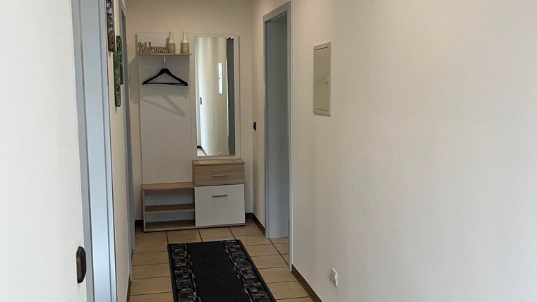 Ein heller Flur mit weißen Wänden und einem langen Teppich. Am Ende des Flurs stehen Schränke und ein Kleiderhaken.
