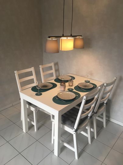Ein helles Esszimmer mit einem weißen Tisch und vier Stühlen. Der Tisch ist schön gedeckt und wird von einer modernen Pendelleuchte beleuchtet.