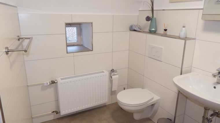 Ein kleines, modernes Badezimmer mit hellen Fliesen. Es enthält ein Waschbecken, eine Toilette und einen Heizkörper.