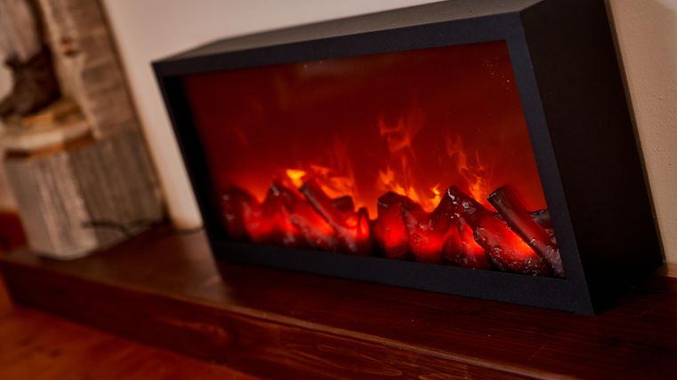 Ein moderner elektrischer Kamin mit flackerndem Feuer und Holzscheiten. Der Kamin verleiht dem Raum eine gemütliche Atmosphäre.