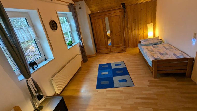 Ein gemütliches Zimmer mit zwei Einzelbetten und einem Holzkleiderschrank. Große Fenster lassen viel Tageslicht herein und der Boden ist mit Holz ausgelegt.