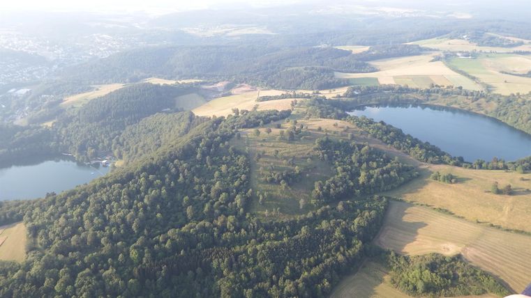 Eine luftige Landschaft mit sanften Hügeln und Wäldern. Zwei Seen sind sichtbar, umgeben von Feldern und Wiesen.