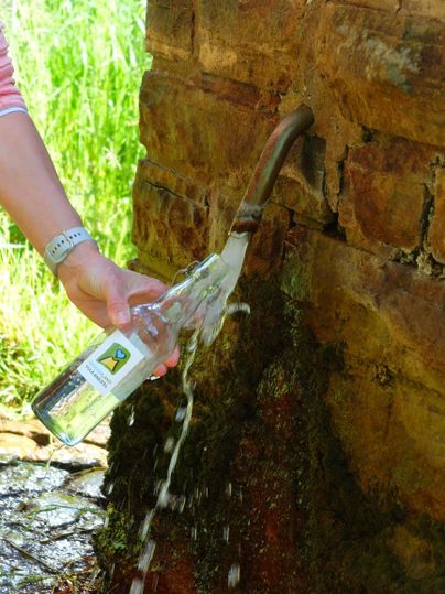 Eine Person füllt eine Flasche mit Wasser aus einem Wasserhahn. Der Wasserfluss ist klar und sprudelnd.