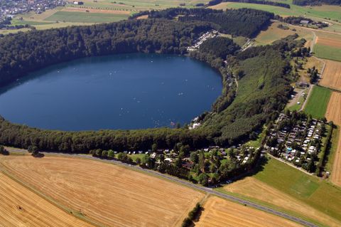 Ein großer, runder See ist von grünen Wäldern umgeben. In der Nähe gibt es Campingplätze und viel freie Landschaft.