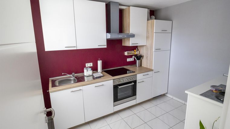 Eine moderne Küche mit weißen Schränken und einer roten Wand. Sie ist gut ausgestattet mit Herd, Backofen und Spüle.