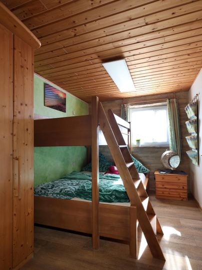 Ein gemütliches Schlafzimmer mit einem Hochbett aus Holz. Die Wände sind grün gestrichen und das Zimmer hat viel Tageslicht.