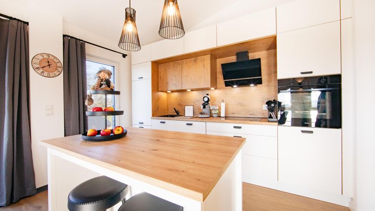 Modern kitchen with a wooden island and elegant chairs. Bright lighting and decorative elements create an inviting atmosphere.