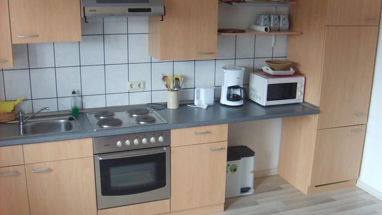 Eine moderne Küche mit Holzschränken und grauer Arbeitsplatte. Es gibt einen Herd, eine Mikrowelle und eine Kaffeemaschine auf der Arbeitsfläche.