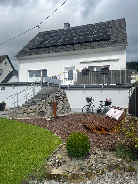 Ein modernes Haus mit Solarpanelen auf dem Dach. Der Garten ist gepflegt, mit einer Steintreppe und einem Fahrrad.