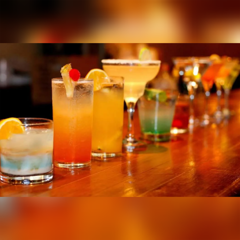 Eine Reihe bunter Cocktails steht auf einer Holzbar. Die Getränke sind in verschiedenen Gläsern mit Früchten und Dekorationen angerichtet.