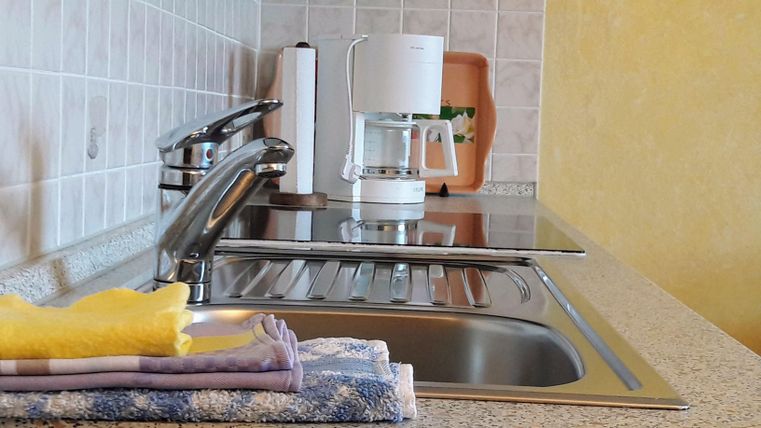 Eine moderne Küche mit einem Waschbecken und einer Kaffeemaschine. Auf der Arbeitsfläche liegen Geschirrtücher.