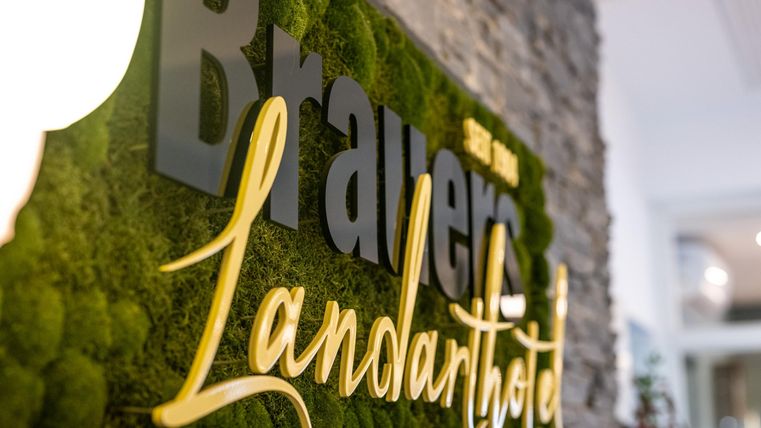Ein ansprechendes Schild mit dem Namen "Landarthotel" in einem grünen Moosdesign. Die Kombination aus Stein und grünen Elementen schafft eine einladende Atmosphäre.