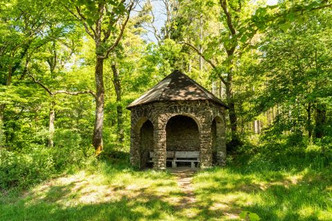 Ein schöner Steinpavillon steht umgeben von üppigem Grün im Wald. Der Ort strahlt Ruhe und Naturverbundenheit aus.