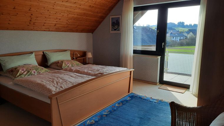Ein gemütliches Schlafzimmer mit einem Doppelbett und sanften Farben. Große Fenster bieten einen Blick auf die Umgebung.