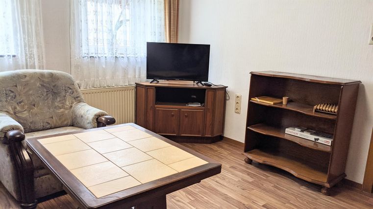 Ein gemütliches Wohnzimmer mit einem Fernseher, einem Tisch und einem Holzregal. Die Einrichtung wirkt einladend und freundlich.