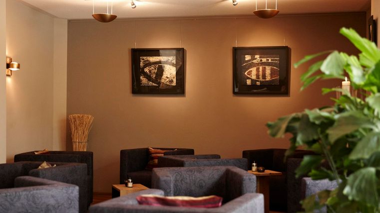 Ein gemütlicher Raum mit blauen Sofas und eleganten Wandbildern. Im Vordergrund eine grüne Pflanze, die eine entspannte Atmosphäre schafft.