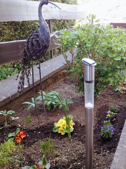 Ein schöner Garten mit bunten Blumen und einem dekorativen Vogel aus Metall. Im Hintergrund steht ein Messgerät für die Bodenfeuchtigkeit.