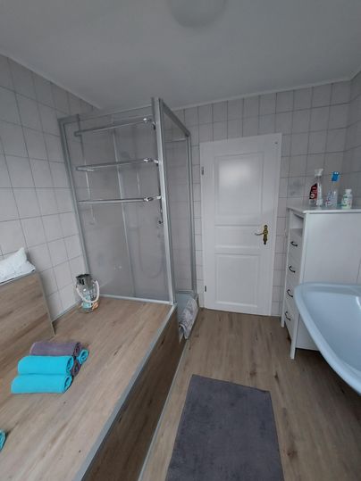 Ein modernes Badezimmer mit einer Duschkabine und einer Badewanne. Die Wände sind hell gefliest, und frische Handtücher sind ordentlich platziert.