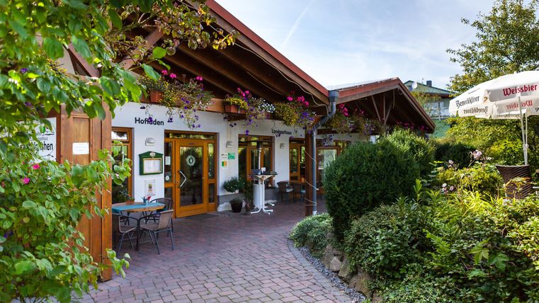 Ein einladendes Restaurant mit einem schönen Eingangsbereich und blühenden Pflanzen. Der gepflasterte Weg führt zur Tür, umgeben von grüner Vegetation.