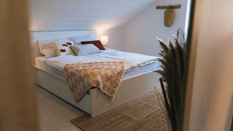 Ein gemütliches Schlafzimmer mit einem großen Bett und weichen Kissen. Der Raum hat warmes Licht und einen natürlichen, einladenden Teppich.